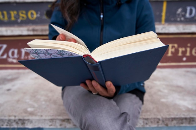 Detail van een opengeslagen boek dat wordt vastgehouden door een vrouw, onscherp weggesneden