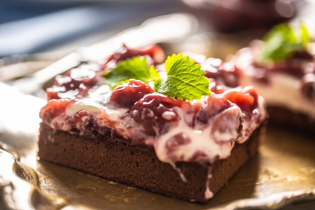 Detail van een stuk brownie met een crème, kersen en verse muntblaadjes.