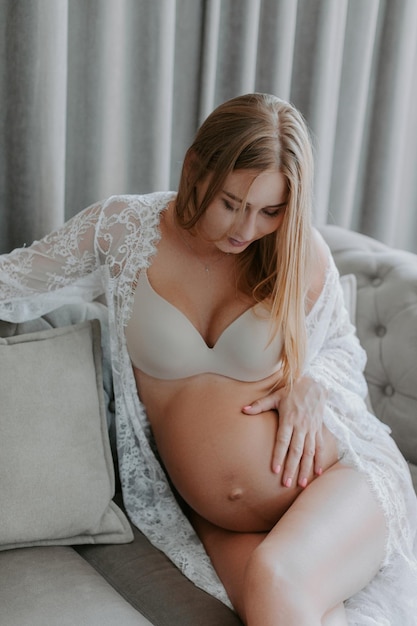 Detail van een zwangere vrouw gekleed in witte kleren, met beide handen de buik vast