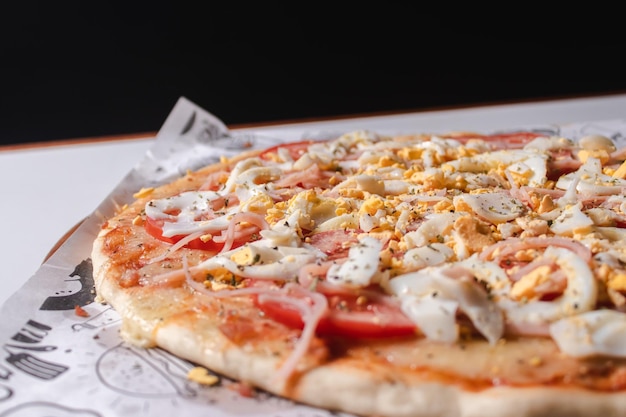 Detail view of a pizza with sliced egg and tomato on a white table