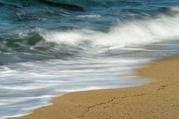 Photo detail view of a wave runs out on a beach the blue color of the sky is reflected in the water