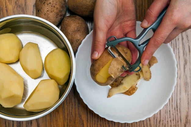 Деталь женщины вручает шелушение свежей желтой картошки с peeler кухни, концепцией приготовления пищи.