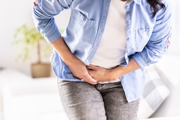 Foto particolare di una donna che soffre di dolori addominali, cistifellea, ovaie, appendice, fegato o intestino tenendo la pancia con le mani.