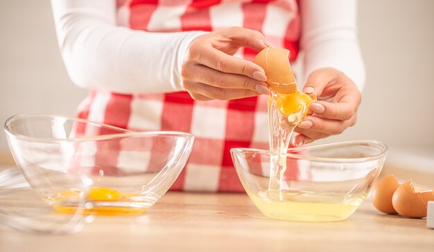 Detail of woman's hands separating egg yolks from the whites into two glass bowls.