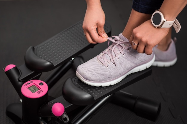 Detail of woman tying her sneakers to train at home with stepper