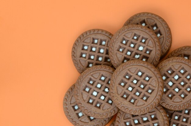 Detailed picture of dark brown round sandwich cookies with coconut filling on an orange surface