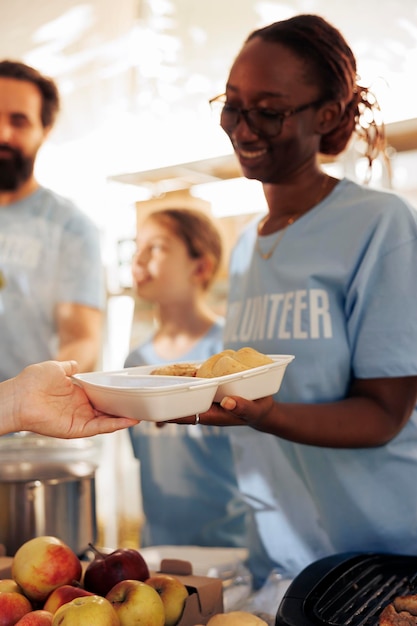 Foto immagine dettagliata mostra volontari che forniscono cibo gratuito agli affamati, ai senzatetto e ai rifugiati. close up di una donna volontaria che distribuisce pasti, fornisce assistenza e condivide prodotti non deperibili.