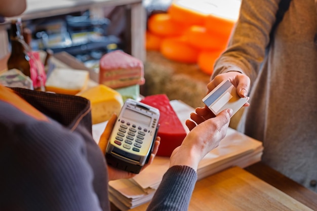 Detailhandel, creditcardbetalingsservice. Klant betaalt voor bestelling van kaas in kruidenierswinkel.