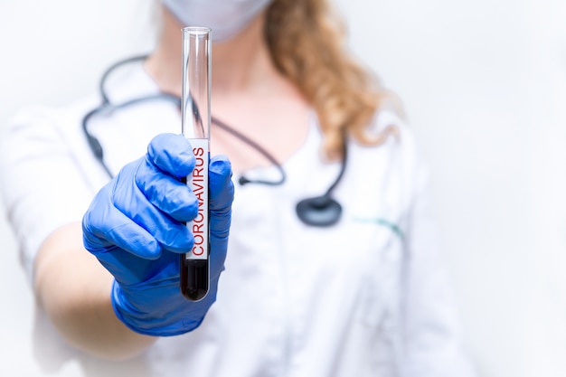 Foto detailopname. een reageerbuis met bloed in de handen van een vrouwelijke viroloog. laboratoriumonderzoek, zoeken naar een vaccin tegen de coronavirusepidemie.