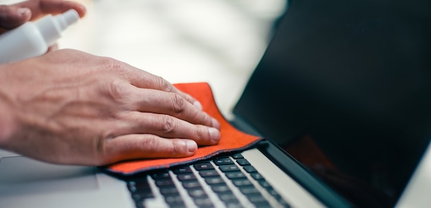 Detailopname. man spuit spray op het oppervlak van een laptop. concept van gezondheidsbescherming