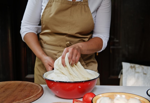 Details chef's handen kneden het verhogen van gistdeeg in een vintage geëmailleerde rode kom tijdens het bereiden van brood in rustieke keuken