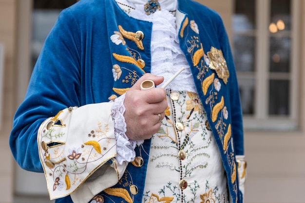 The details of man dressed in a baroque costume a hand holding a pipe golden buttons vest