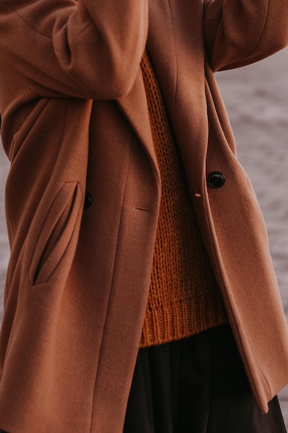 Foto dettagli del maglione femminile arancione caldo e accogliente e del cappotto marrone collezione autunno inverno street style