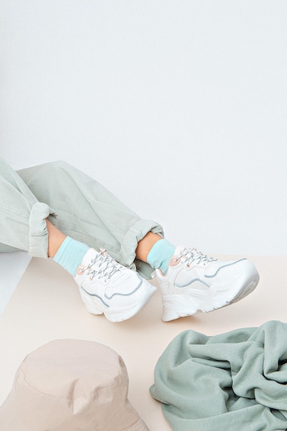 Details of trendy casual spring summer fresh outfit. Girl in studio wearing khaki jeans and stylish white sneakers.  Bucket hat and sweater. No face. Minimalist vegan clothing concept