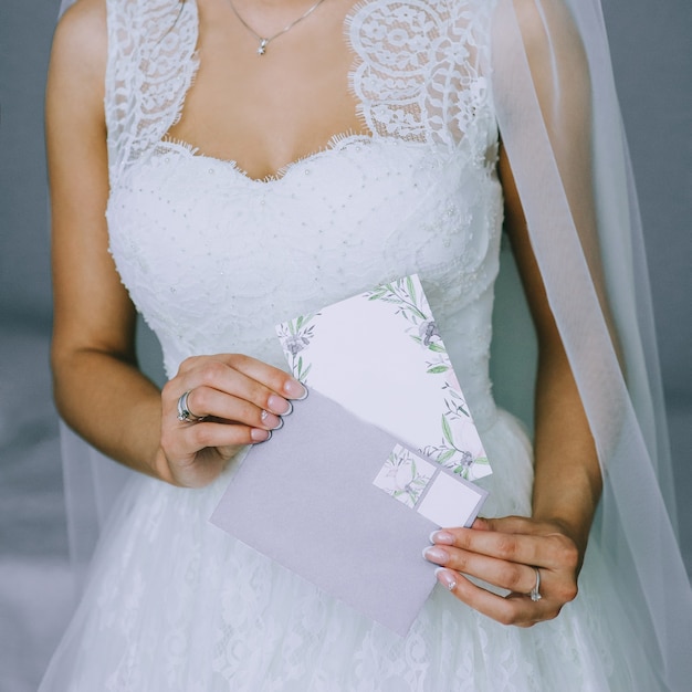 Details van een trouwjurk. Close up van anonieme meisje in mooie witte trouwjurk met een envelop met een lege briefkaart. Bruidstoebehoren. Ochtend van de bruid.
