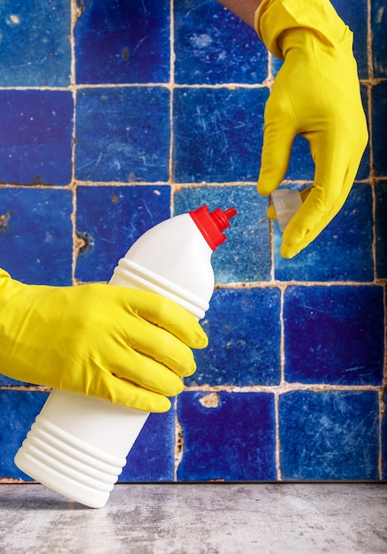 黄色の手袋をはめた手に洗剤ボトルがあり、トイレとバスルームの洗浄ジェル液体を開きます