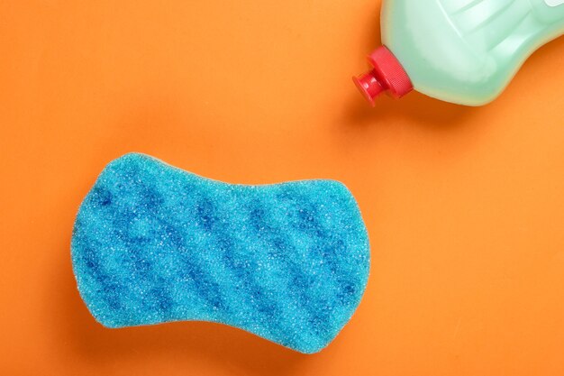 Detergent bottle and sponge on orange background