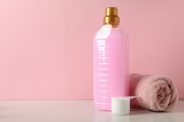 Detergent, scoop with powder and towel on white table against pink