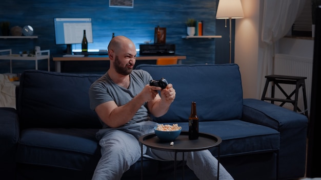 Determinated excited man sitting on sofa playing video games