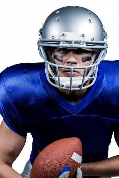 Determined American football player in uniform holding ball