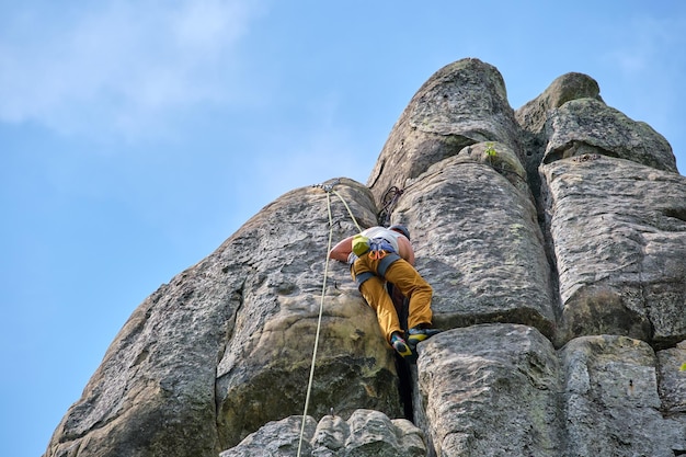 Determined climber clambering up steep wall of rocky mountain Sportsman overcoming difficult route Engaging in extreme sports and rock climbing hobby concept