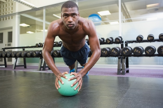 Determined man doing push ups with ball in gym