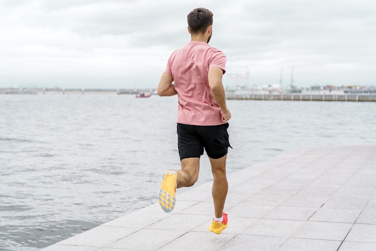 Photo a determined man in a pink shirt and black shorts jogs along a waterfront promenade