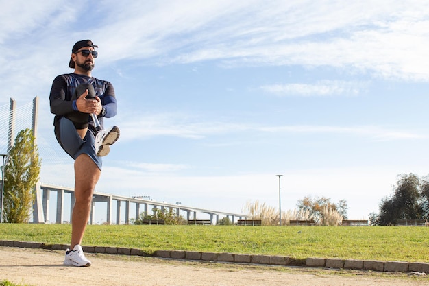 写真 ジョギングの準備をしている義足を持つ決心した男。夏の日に公園でストレッチ、運動しているスポーツ服を着た男。スポーツ、トレーニング、幸福、障害の概念