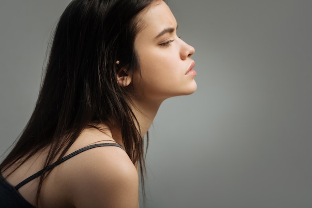 Determined. Pretty stony-faced long-haired young woman thinking and looking in the distance and wearing a top