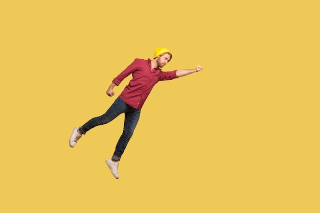 Determined serious ambitious guy flying in air with raised\
hand, striving forward to victories, feeling super hero power,\
freedom and confidence to achieve goal. indoor studio shot, yellow\
background