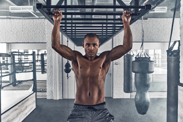 Determined to win. Shirtless young African man looking at camera and doing pull-ups 