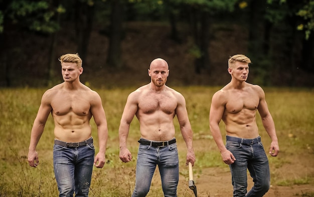 Foto determinato a vincere tre uomini muscolosi con l'ascia, l'uomo atletico usa l'ascia, ragazzi sexy maschi brutali e forti, sei confezioni e il concetto di bodybuilding di proteine o steroidi per bicipiti si rilassa dopo il lavoro nella foresta