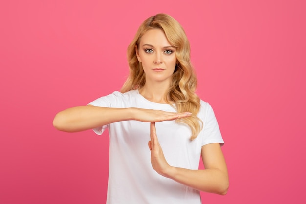 Foto giovane donna bionda determinata che mostra il gesto del time-out su uno sfondo rosa