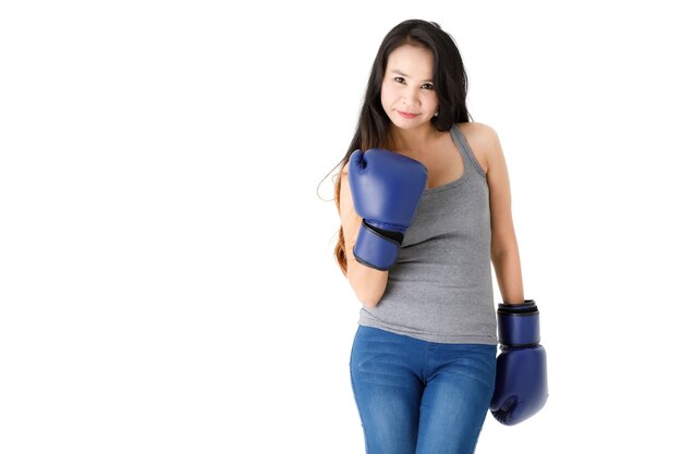 Determined young fit Asian female in blue boxing gloves standing in fighting stance and looking at camera with smile against white background