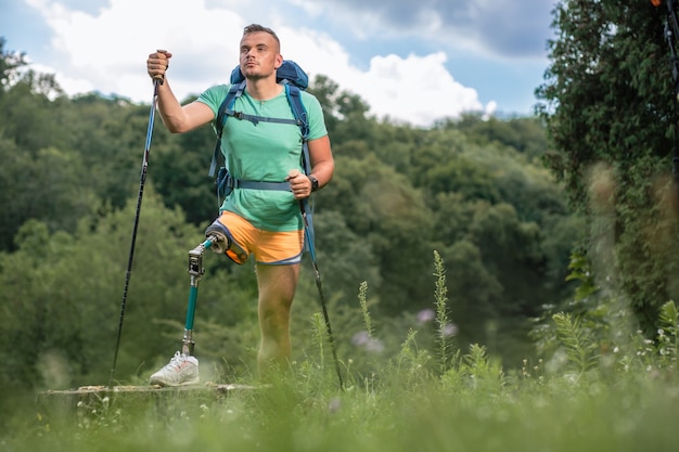 Determined young male tourist with prosthesis trying Nordic walking while enjoying his active weekend