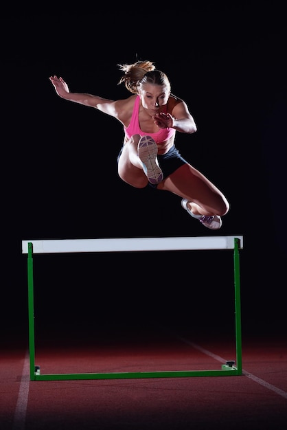Determined young woman athlete jumping over a hurdles