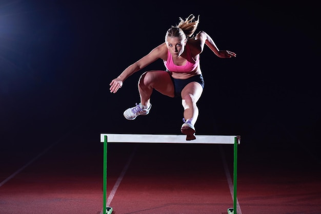 Determined young woman athlete jumping over a hurdles