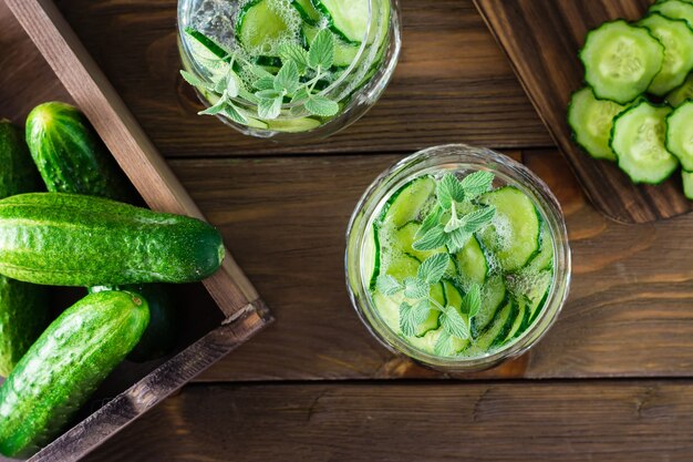 Detox drink. Water with pieces of cucumber and ice in a transparent glass on a wooden table. Top view