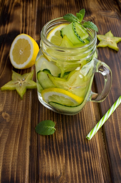 Detox or infused water with cucumber, carambola and lemon on the brown wooden background