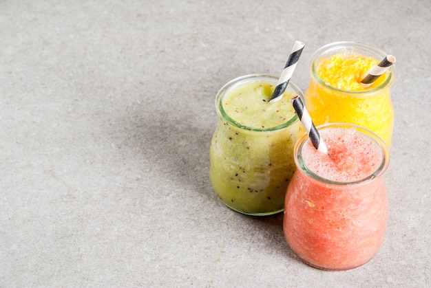 Detox organic diet drinks, homemade tropical smoothies - kiwi, orange, grapefruit, in portioned jars, on a gray stone table. Copy space