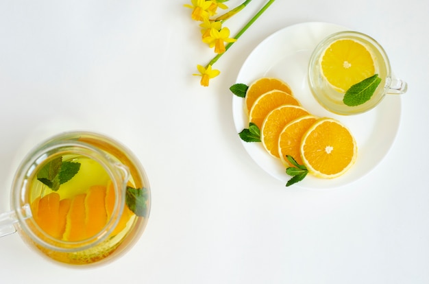 Detox tea in transparent teapot with orange fruit and mint and yellow Narcissus flower