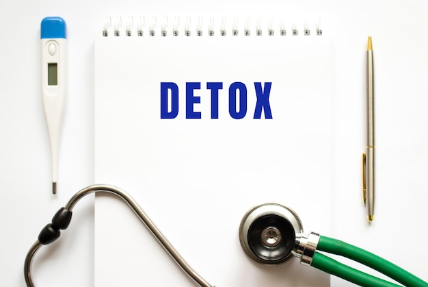 DETOX text written in a notebook lying on a desk and a stethoscope