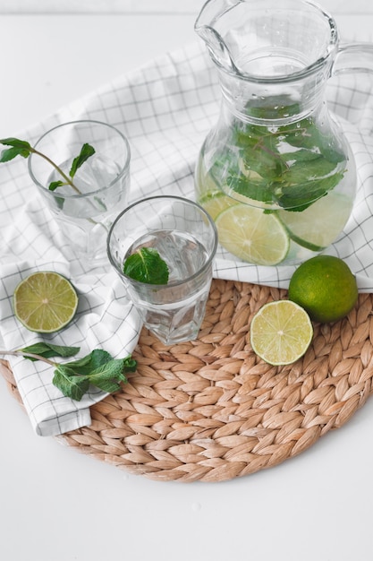 Detox water with lime fruit and mint leaves in jar and glasses