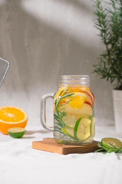 Detox water with lime organe apple and rosemary in a mason jar glass with a white wooden background