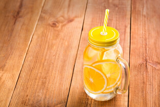 detox water with orange slices in a glass jar with a handle, lid and straw