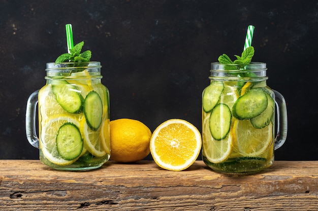 Detox water with sliced lemon and cucumber in a jar on dark.