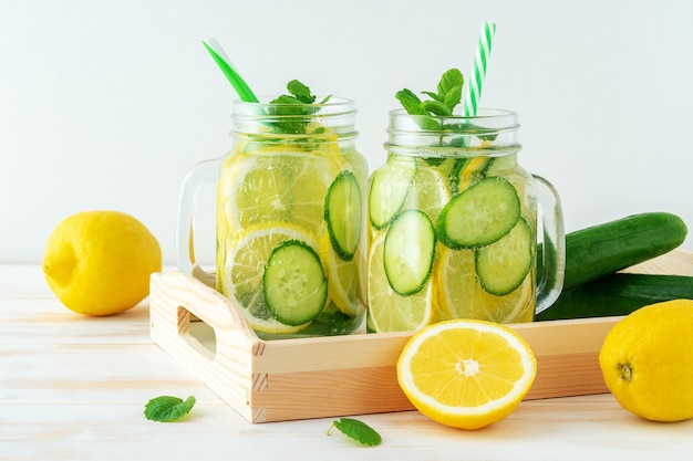 Detox water with sliced lemon and cucumber in a jar on wooden table.