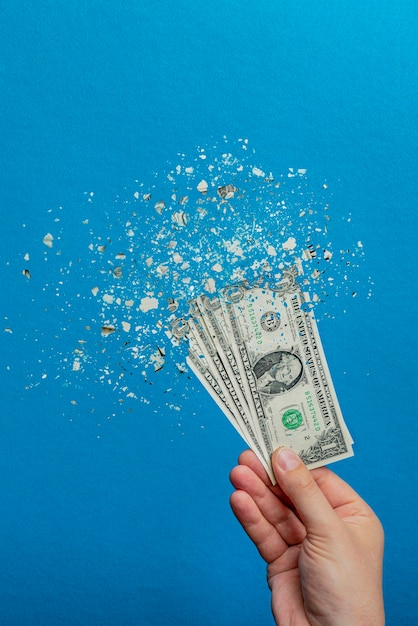 Devaluation of money. Printing money leads to inflation. Decrease in the value of the American currency, dollar. Dollar bill breaks up into particles on a blue background