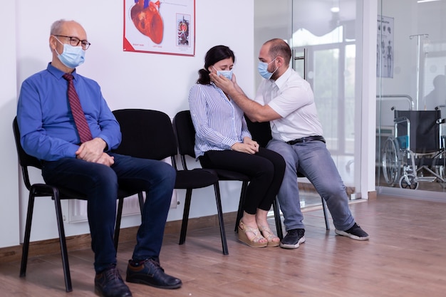 Devastated wife crying in hospital waiting room wearing protection mask while waiting news from doctor