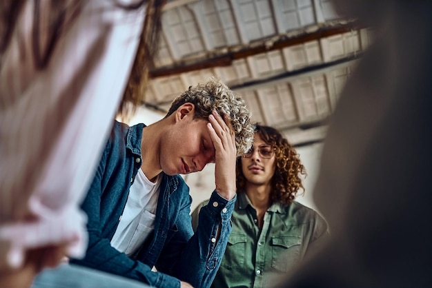 devastated young man holding his head in his hands group of friends in supportive pose around him